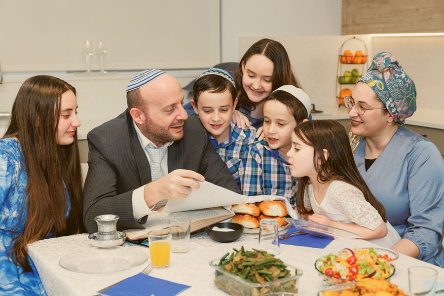 משפחה יושבת סביב שולחן השבת ומתבוננת בדפי אגדת השבוע